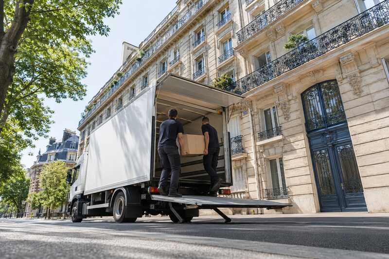 Camion de déménagement, hayon déployé, devant un immeuble en pierre de taille