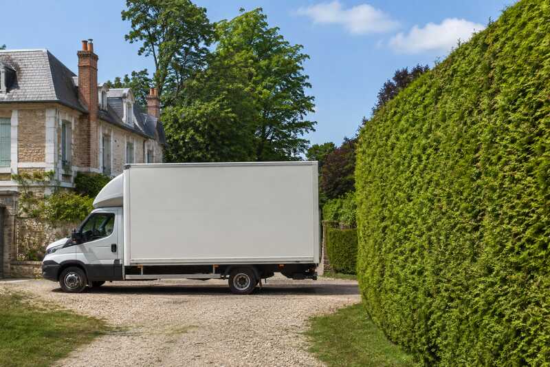 Camion de déménagement reculant dans l’allée d’un pavillon en lisière de bois