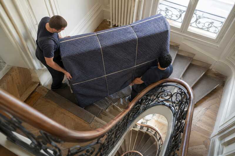 Piano protégé guidé dans un escalier ancien à rampe de fer forgé